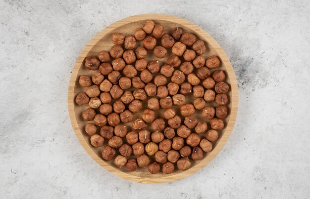 Round plate of organic hazelnut kernels on marble table. 