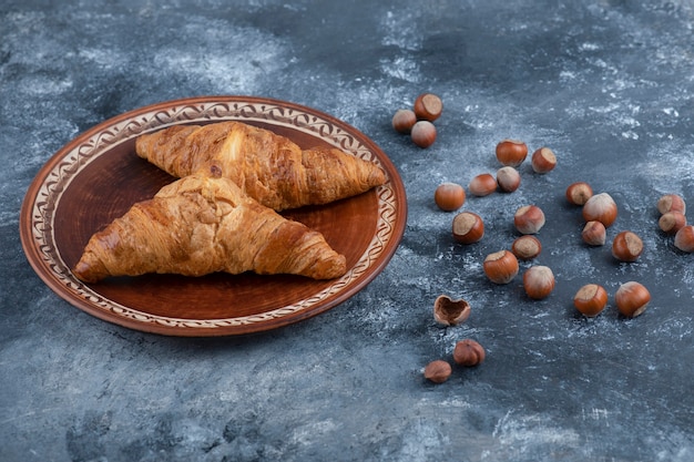 A round plate with fresh croissants and healthy macadamia nuts.