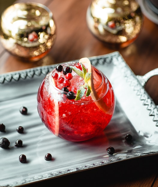 Round-shaped glass of berries cocktail garnished with lemon slice