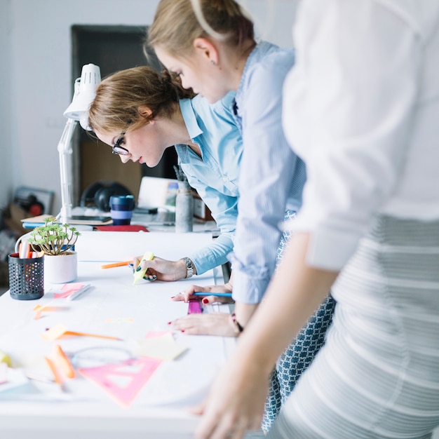 Free photo row of businesswomen drawing project on white paper at workplace