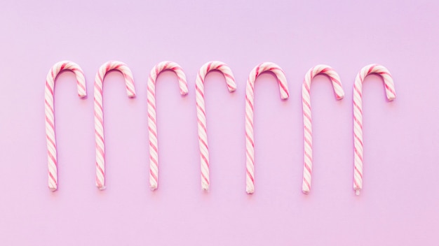 Free photo row of christmas peppermint cane candies on pink background