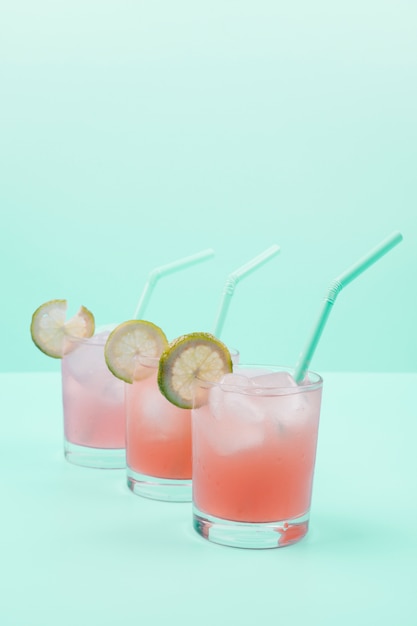 Row of cocktail glasses with ice cubes; drinking straw; lemon slices on mint background