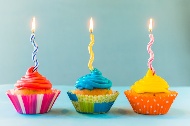 Row of cupcakes with burning candles on blue backdrop