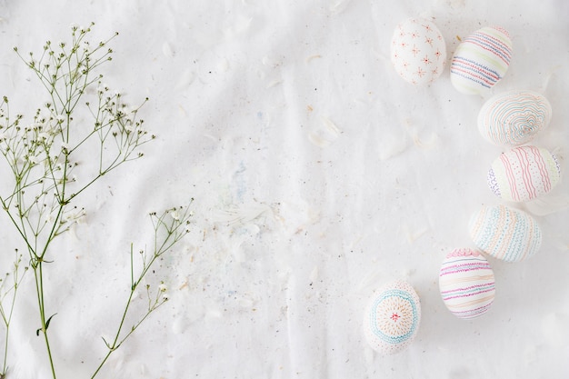 Row of Easter eggs with patterns near plant twig and feathers on textile