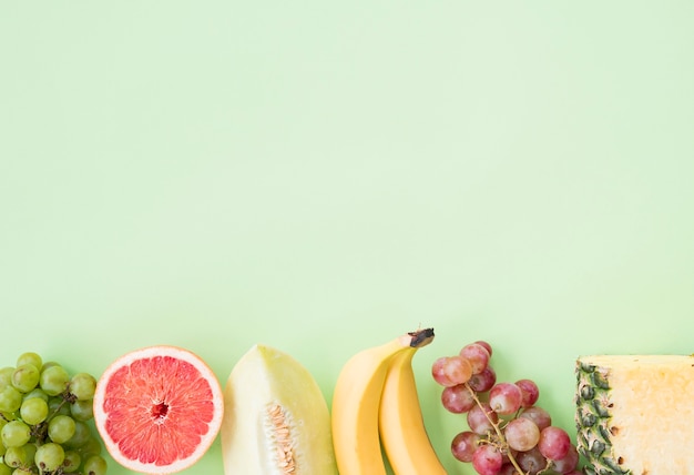 Row of grapes; grapefruit; muskmelon; banana; grapes and pineapple on pastel background