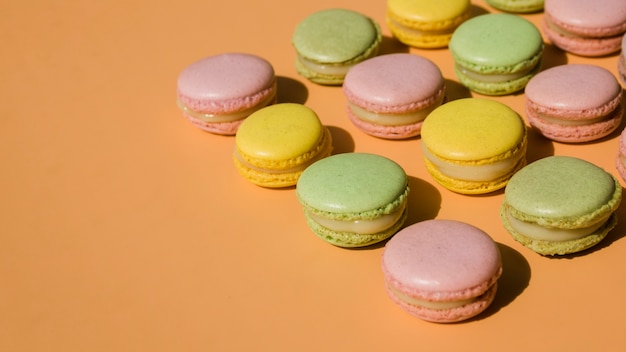 Free photo row of pink; green and yellow macaroons on beige backdrop