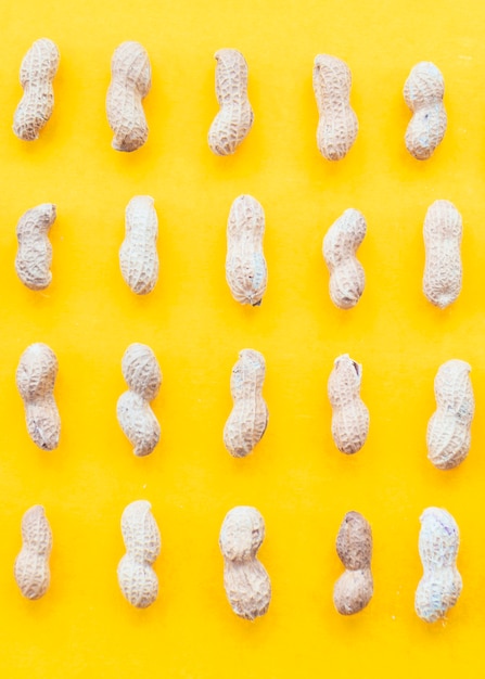 Free Photo row of raw peanuts on yellow backdrop