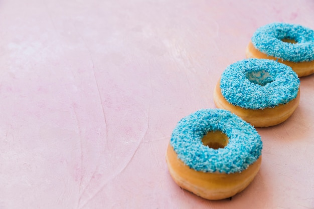 Free photo row of three blue donuts in a row on pink background