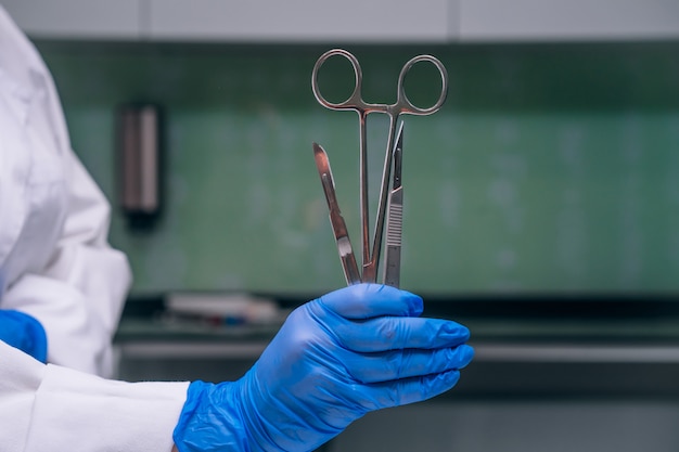 Free Photo a rubber gloved hand holds two scalpels and a clamp