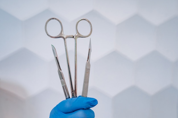 A rubber gloved hand holds two scalpels and a clamp