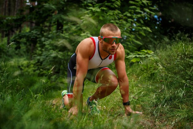 Runner man in sunglasses ready for quick start in the forest.