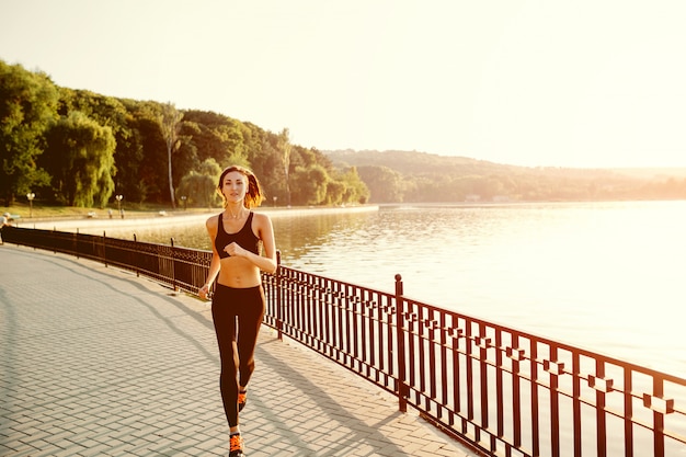 Running woman. Runner jogging in sunny bright light. Female fitness model training outside in park