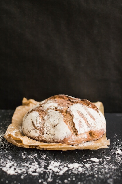 Free photo rustic homemade baked bread on brown paper against black background