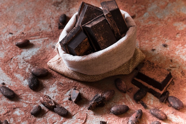 Free Photo sack of chocolate bar pieces and cocoa powder and beans on table