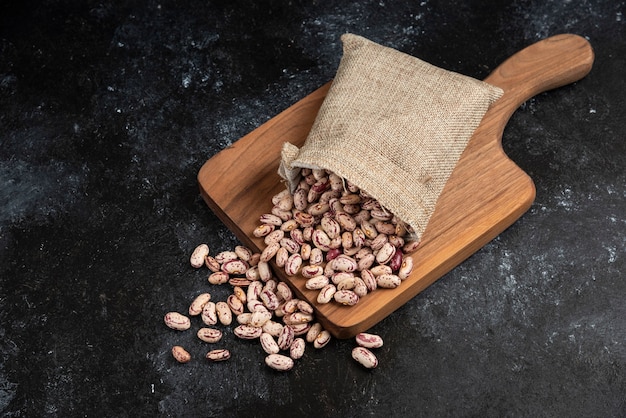 Sackcloth of dried raw beans placed on wooden board. 