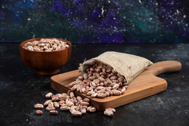 Sackcloth of dried raw beans placed on wooden board. 