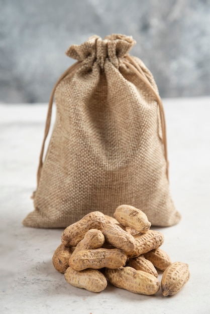 Free photo sackcloth of organic roasted peanuts placed on marble table.