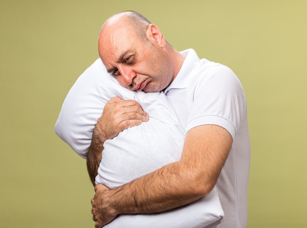 sad adult ill caucasian man holding and putting head on pillow isolated on olive green wall with copy space