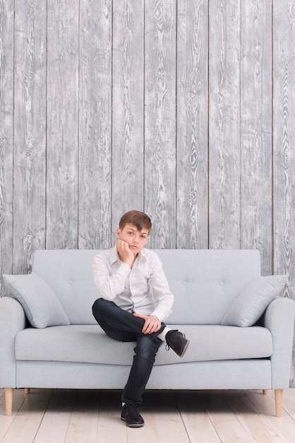 Sad boy sitting on sofa at home looking at camera