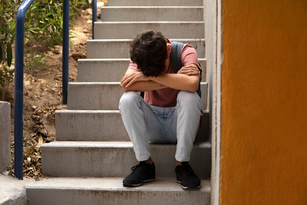 Sad boy sitting on stairs full shot