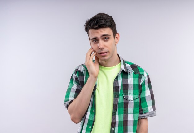 Sad caucasian young guy wearing green shirt put his hand on aching tooth on isolated white background