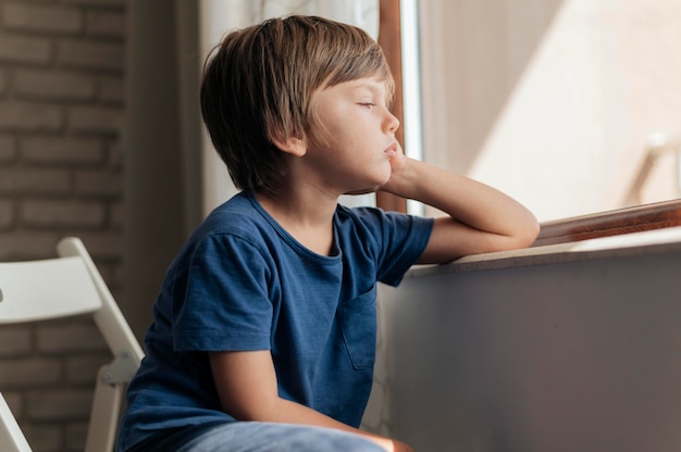 Sad child looking through the window during quarantine