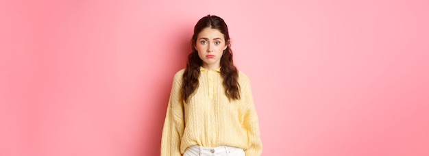 Free photo sad cute woman looking innocent and silly at camera standing against pink background