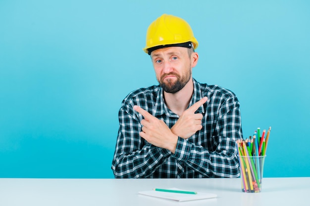 Sad engineer man is crossing hands on blue background