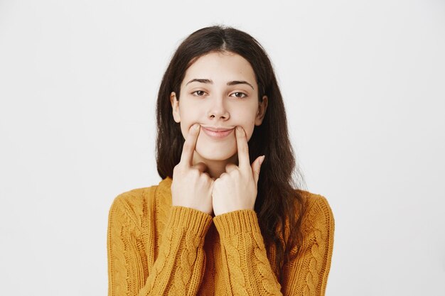 Sad girl trying pull happy smile, pushing lip corners upwards with reluctant face