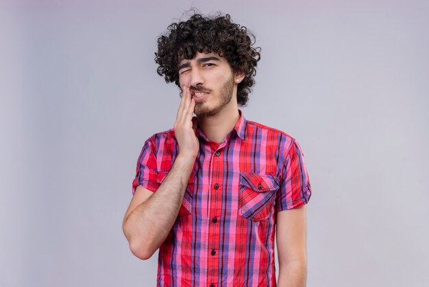 A sad handsome man with curly hair in checked shirt feeling ache on teeth 