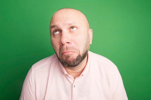 Sad looking up middle-aged bald man wearing pink t-shirt isolated on green