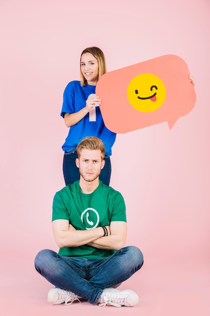 Free photo sad man sitting in front of happy woman holding winking emoji speech bubble