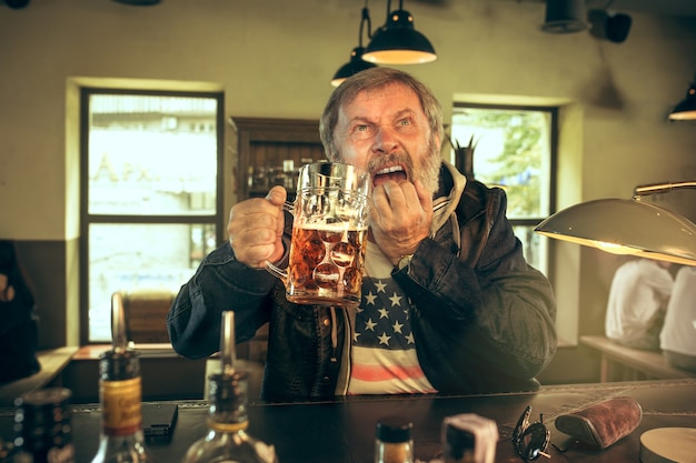 Free photo the sad senior bearded male drinking beer in pub