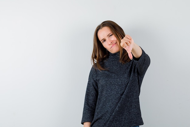 Free Photo the sad woman is pointing down with her thumb on white background