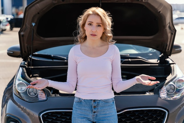 Sad woman standing next to her broken car