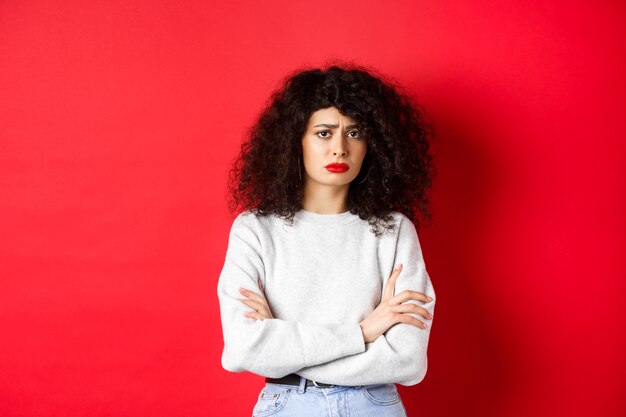 Sad and worried caucasian woman frowning cross arms on chest and looking concerned feeling bad stand...