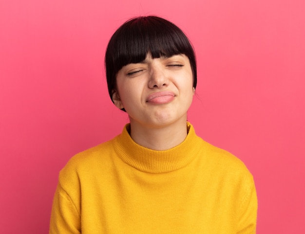 Sad young brunette caucasian girl stands with closed eyes on pink