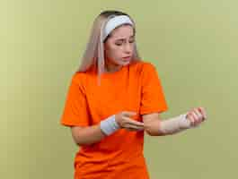 Free photo sad young caucasian sporty girl with braces wearing headband and wristbands points and looks at hand