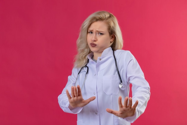 Sad young doctor wearing stethoscope in medical gown showing no gesture on red backgroung