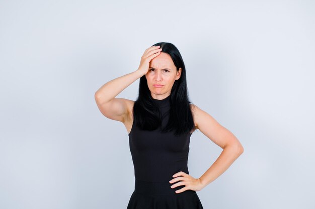 Sad young girl is putting one hand on head and other on waist on white background