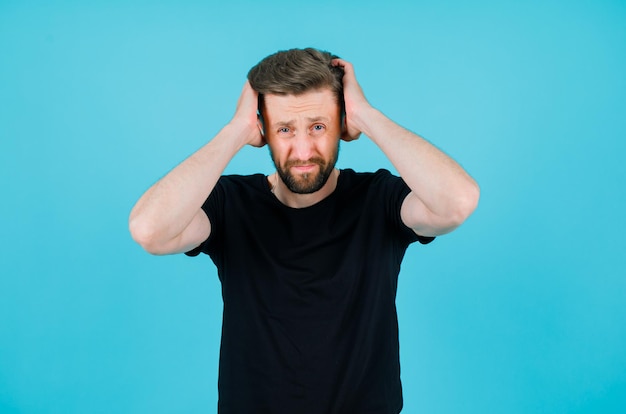 Free photo sad young man is putting hands on head on blue background