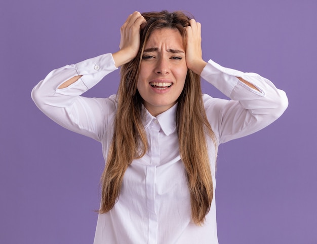 Sad young pretty caucasian girl puts hands on head isolated on purple wall with copy space