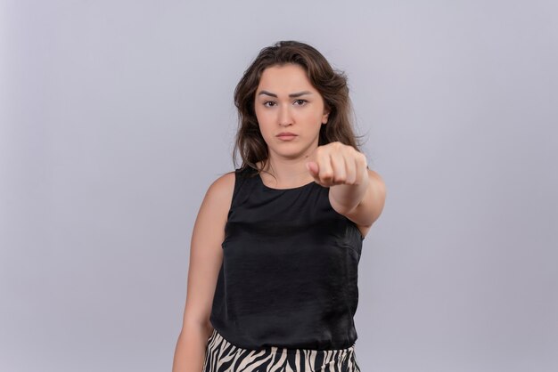 Sad young woman wearing black undershirt held out fist to forward on white wall