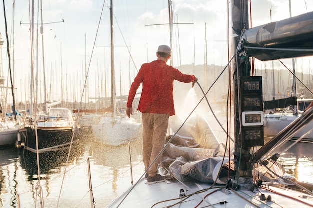 Free Photo sailboat owner or yachtsman uses hose to wash of salt water from yachr deck when docked or parked in marina on sunset