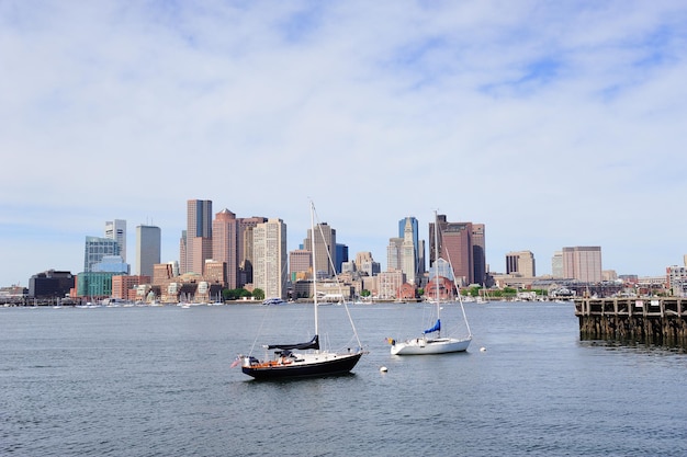 Sailing boat rest with dock in bay and Boston downtown skyline with urban skyscrapers over sea in the morning.