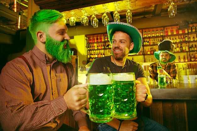 Saint Patrick's Day Party. Happy friends are celebrating and drinking green beer. Young men and women wearing green hats. Pub Interior.