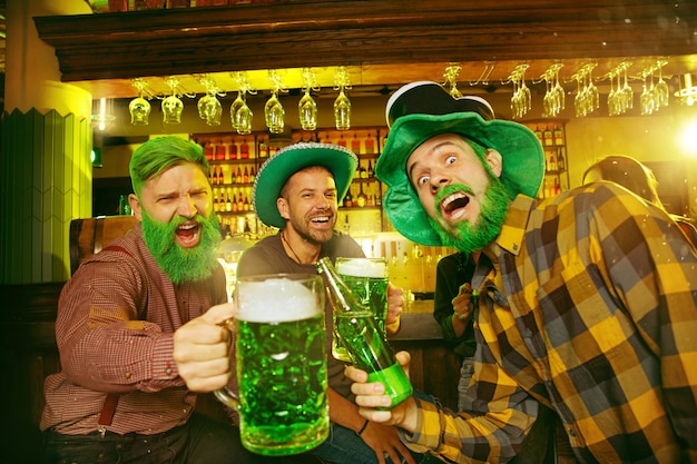 Saint Patrick's Day Party. Happy friends are celebrating and drinking green beer. Young men and women wearing green hats. Pub Interior.