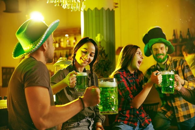 Saint Patrick's Day Party. Happy friends are celebrating and drinking green beer. Young men and women wearing green hats. Pub Interior.