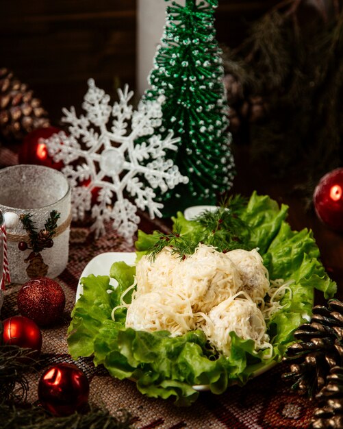 Salad balls covered in grated cheese served in bowl decorated with lettuce