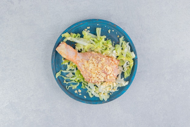 Free photo salad and chicken leg in the wooden plate , on the blue surface